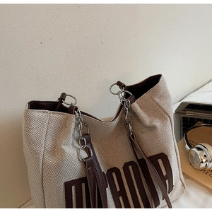 Detail of canvas tote bag showing large printed letters and leather chain strap