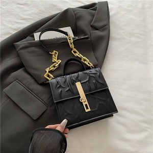 Black textured square chain crossbody bag with gold hardware on a dark grey suit jacket