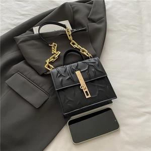 Black square crossbody bag with branch texture and gold chain decoration on blazer