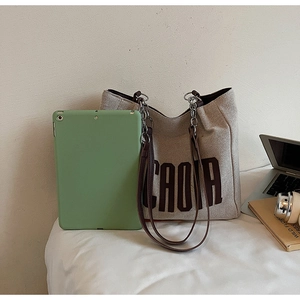 Detail of canvas tote bag showing large brown letters, leather straps, and metal chains