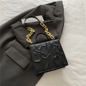 Chic black square bag with embossed texture and bold gold chain strap on grey blazer