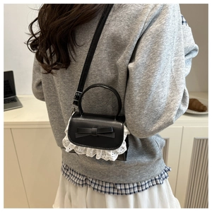 Dettaglio mini borsa nera con fiocco e pizzo bianco indossata a spalla da modella