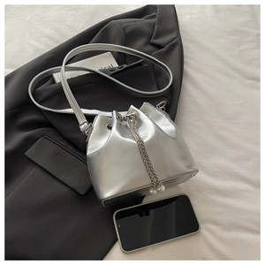 Detail of silver metallic bucket bag with chain strap and pearls beside a smartphone