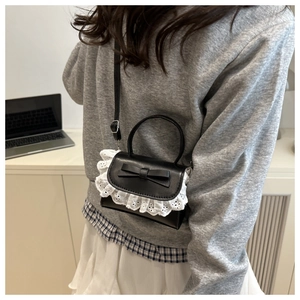 Detail of a black leather crossbody bag featuring white lace trim and bow decoration