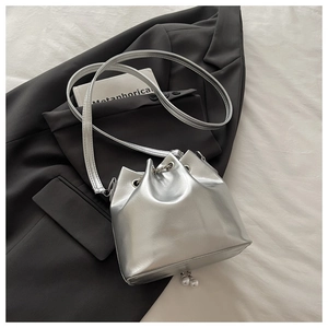 Close-up of metallic bucket bag with pearl charms on a grey blazer background