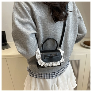 Close-up of black mini leather crossbody bag with lace trim and bow on a model's back