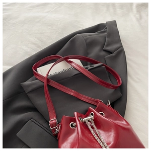 Detail of red glossy bucket bag with silver chain drawstring on a grey blazer