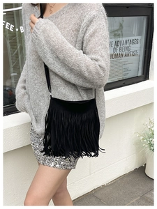 Close-up of black suede shoulder bag featuring long fringe detail on a street style model