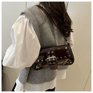 Detail of a shiny brown lacquer baguette bag with silver studs and metal buckle on a model