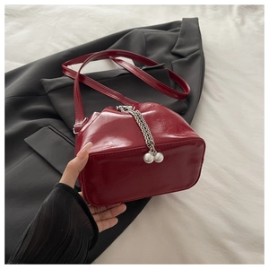 Detail of burgundy glossy bucket bag with large pearl charms and metal chain decoration