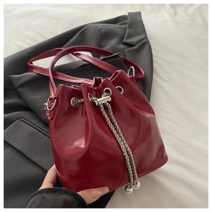 Detail of red patent leather bucket bag with silver chain and pearl drawstring on black suit