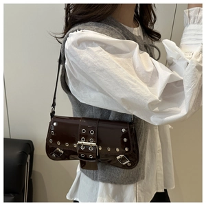 Detail of dark brown patent leather shoulder bag with punk metal eyelets and rivets
