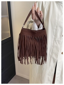Close-up of deep brown suede handbag with fringe tassels held against a beige coat