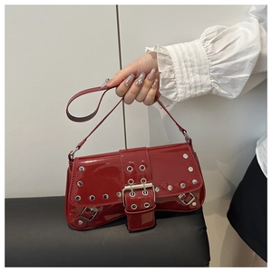 Close-up of red patent leather shoulder bag featuring silver rivets and a buckle strap