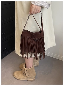 Detail shot of brown matte shoulder bucket bag featuring long bohemian tassels and strap