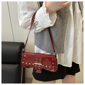 Detail view of red patent leather underarm bag with silver grommets and punk style buckles