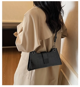 Detailed view of a black crocodile-pattern baguette bag worn with a beige trench coat