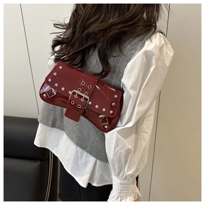 Macro view of burgundy patent leather baguette bag with silver rivets and buckle