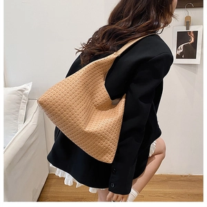 Close-up of khaki woven hobo bag with wide shoulder strap worn by model in black suit