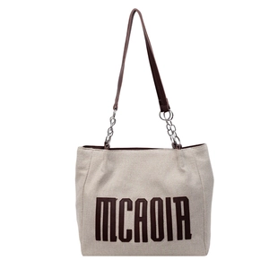 Large beige canvas tote bag with brown leather strap and metal chain detail