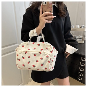 Close-up of cream corduroy tote bag featuring red strawberry prints and front zipper pocket