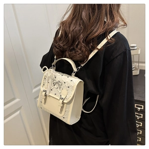 Détail d'un sac à dos en dentelle beige avec nœuds noirs et breloques en perles