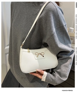 Close-up of white underarm bag featuring a gold metal bow and floral zipper charm