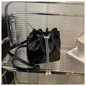 Detail of black patent leather bucket bag with silver chain drawstring and pearl charm