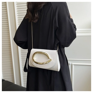 Modern white flap shoulder bag with gold hardware worn over a chic black long coat