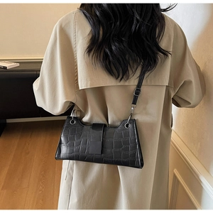 Detail of black crocodile pattern baguette bag with adjustable strap on model's shoulder