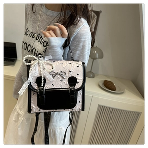 Détail d'un sac bandoulière rose et noir avec nœud en dentelle et chaîne de perles élégante