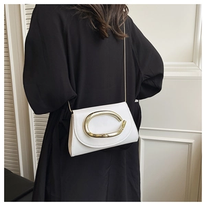 Détail du sac carré blanc avec boucle dorée et chaîne en métal porté sur un manteau noir