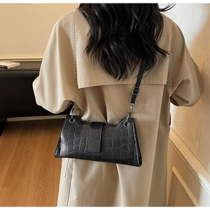 Detail of a black croc-embossed baguette shoulder bag worn over a beige trench coat