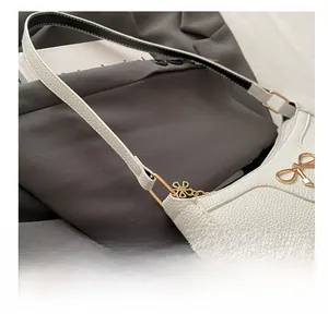 Detailed close-up of white pebbled leather handbag with gold metal bow buckle