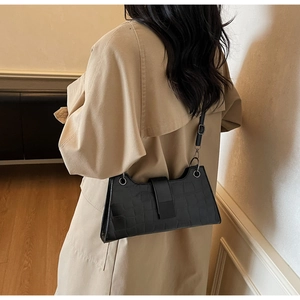 Detail of black crocodile pattern baguette bag worn with a stylish beige trench coat
