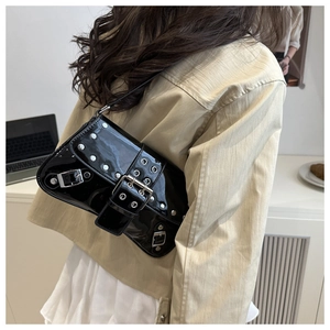 Model wearing a black patent leather punk shoulder bag with silver studs and metal buckle