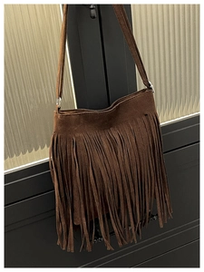 Detailed view of dark brown suede shoulder bag featuring long bohemian tassels and hardware
