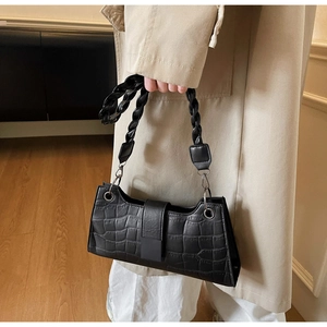 Detail of black crocodile pattern baguette bag with woven handle and magnetic closure