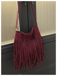 Detail of burgundy suede shoulder bag featuring long tassels and silver metal buckle