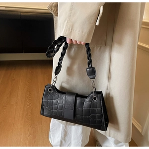 Detail of black crocodile texture baguette bag featuring a woven handle and metal buckle