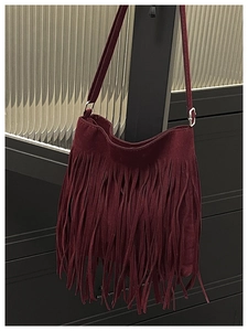 Detail of dark burgundy faux suede crossbody bag featuring long bohemian style fringe