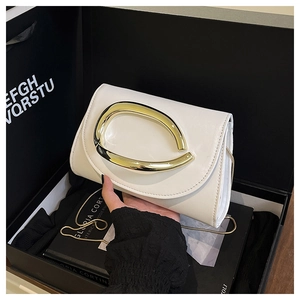 Détail d'une pochette de soirée en cuir crème avec boucle dorée et chaîne dans un coffret