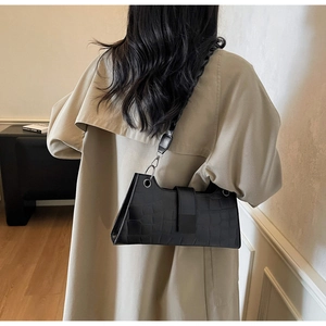 Detail of black crocodile pattern rectangle shoulder bag with wide strap on a model