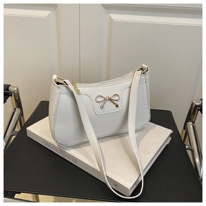Close-up of white pebble leather baguette bag featuring a gold metal bow ornament