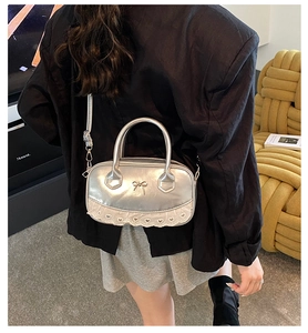 Detail der silbernen Boston Bag mit Spitze und Schleife auf einem dunklen Blazer