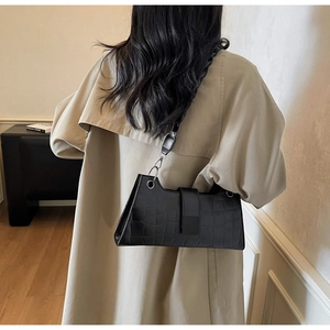 Close-up of black crocodile pattern baguette bag with silver ring detail on shoulder