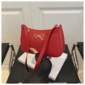 Detail of red pebbled leather baguette bag with a golden metal bow buckle and slim strap