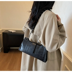 Detail of black crocodile texture baguette bag featuring a wide flap and metal eyelets