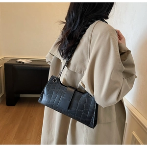 Detail of black crocodile texture baguette bag shown on a beige trench coat