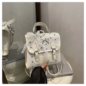 Détail d'un sac à dos crème avec texture plissée, nœuds noirs et breloques en perles